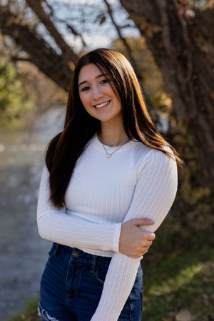 Portrait series in white sweater against autumn trees and water backdrop.