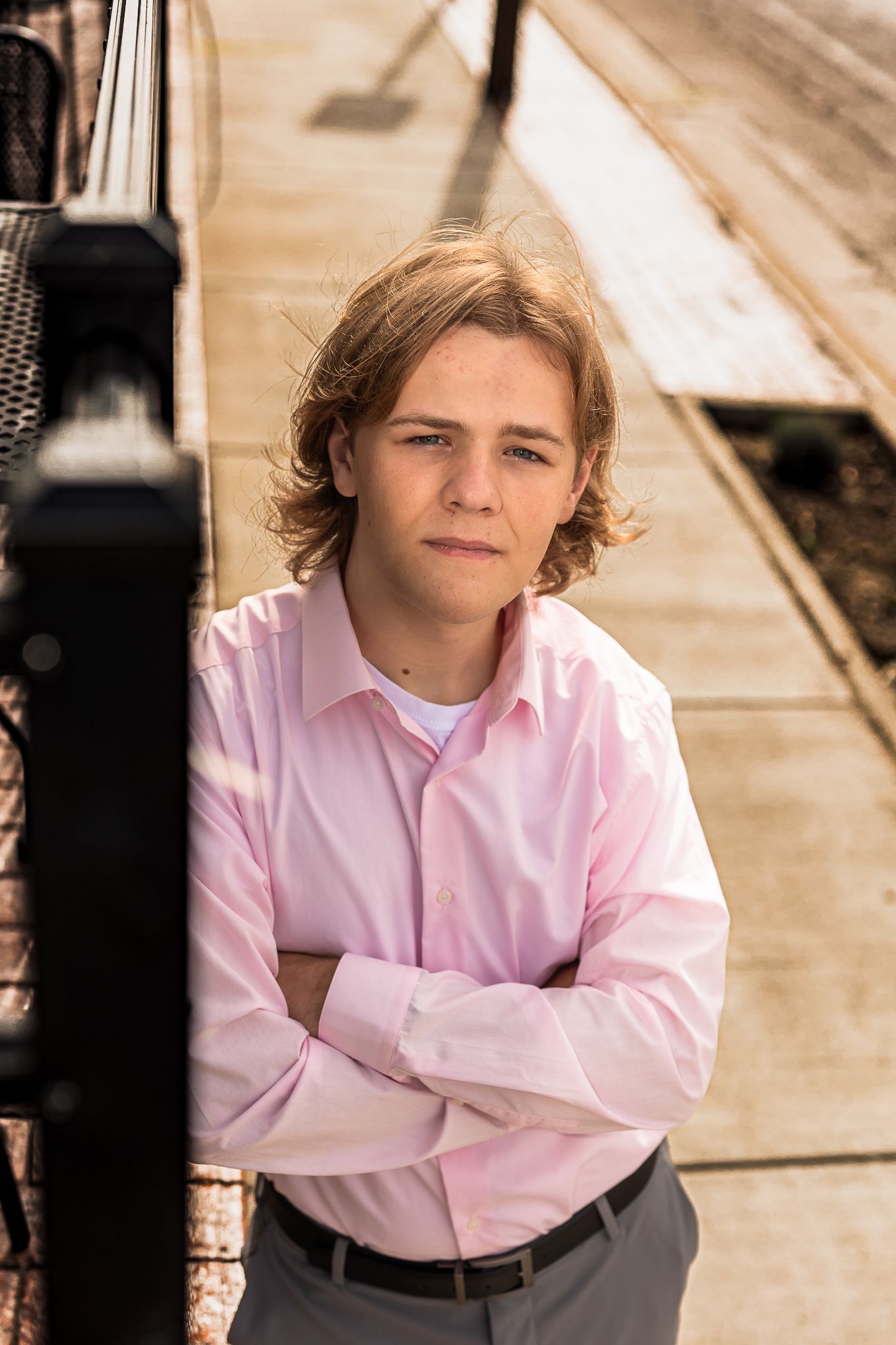 Person in pink shirt posing against metal railing with warm lighting.