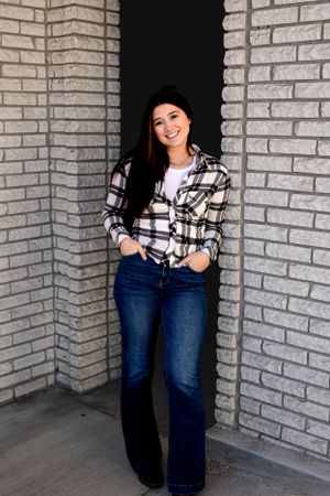 Portrait session against grey brick wall wearing plaid shirt and jeans.