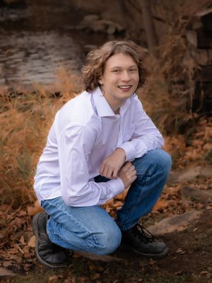 Person in white button-down shirt and jeans sitting casually on autumn ground.