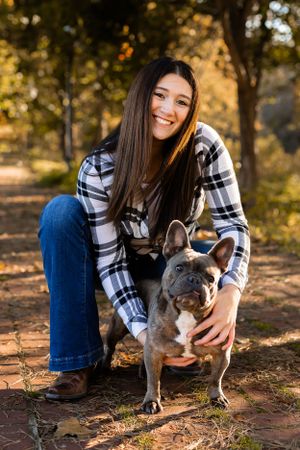 French bulldog puppy plays outdoors with owner in plaid shirt and jeans during autumn photoshoot.