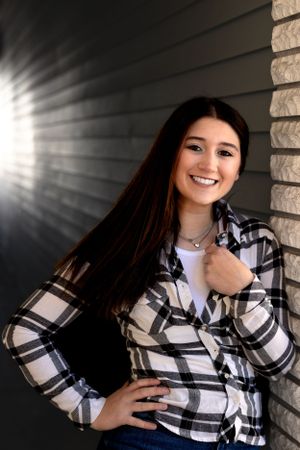 Person in plaid shirt poses near brick wall with dramatic lighting.