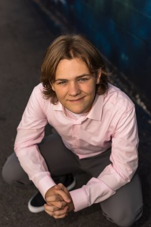 Person in pink dress shirt lying on dark surface in studio setting.