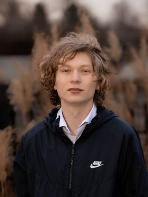Person wearing black Nike jacket and white shirt poses against natural background.