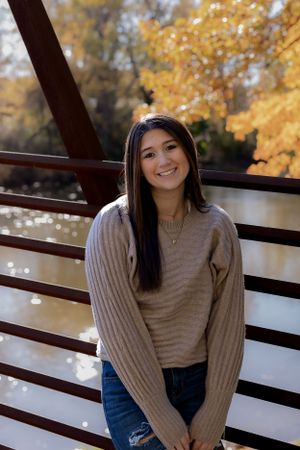 Casual portraits taken on wooden bridge with fall foliage and water in background.