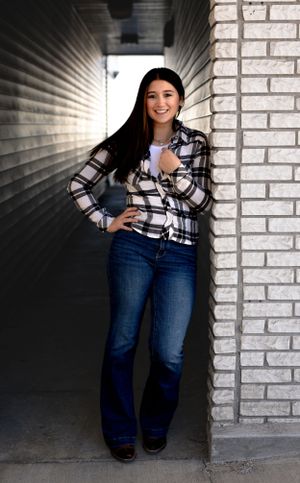 Person wearing plaid shirt and jeans sits casually against white brick wall.