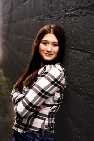 Person in plaid shirt smiles while posing against black wall.