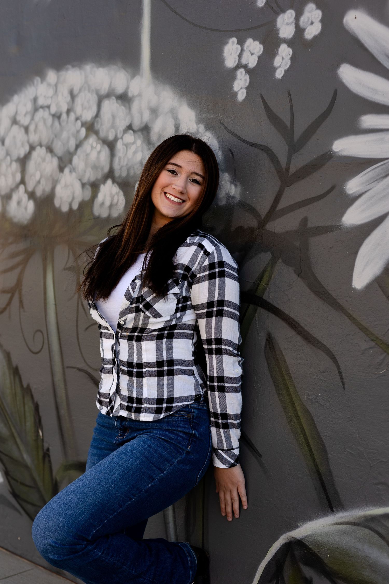 Portrait against gray wall with white floral mural wearing plaid shirt and jeans.