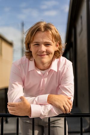Person in pink shirt leaning on black railing outdoors.