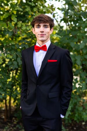 A series of formal portraits showing a person in a black suit with a red bowtie against a leafy green background.