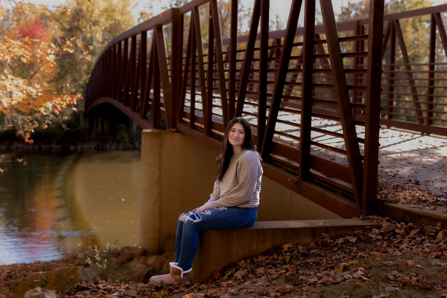 Person sitting on wooden bridge during autumn with colorful fall foliage in background.