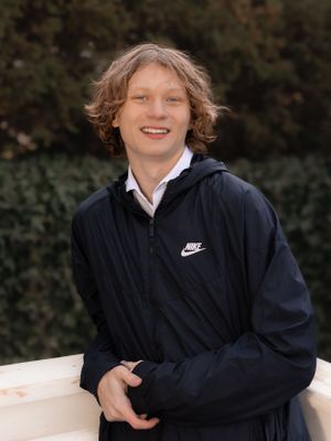 Person in Nike hoodie and white shirt poses on white bench outdoors.
