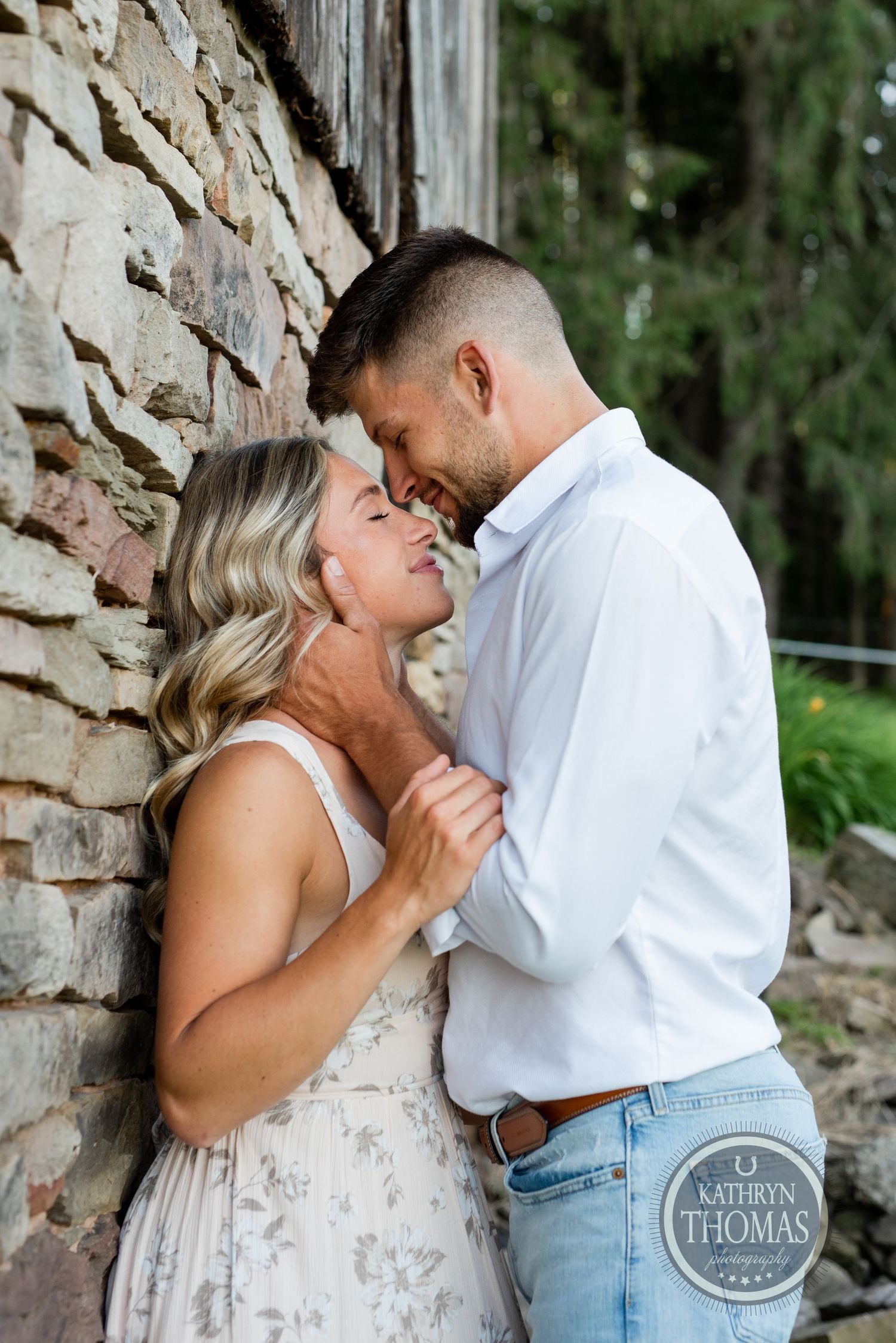 An intimate portrait of a couple sharing a close moment against a weathered stone wall.