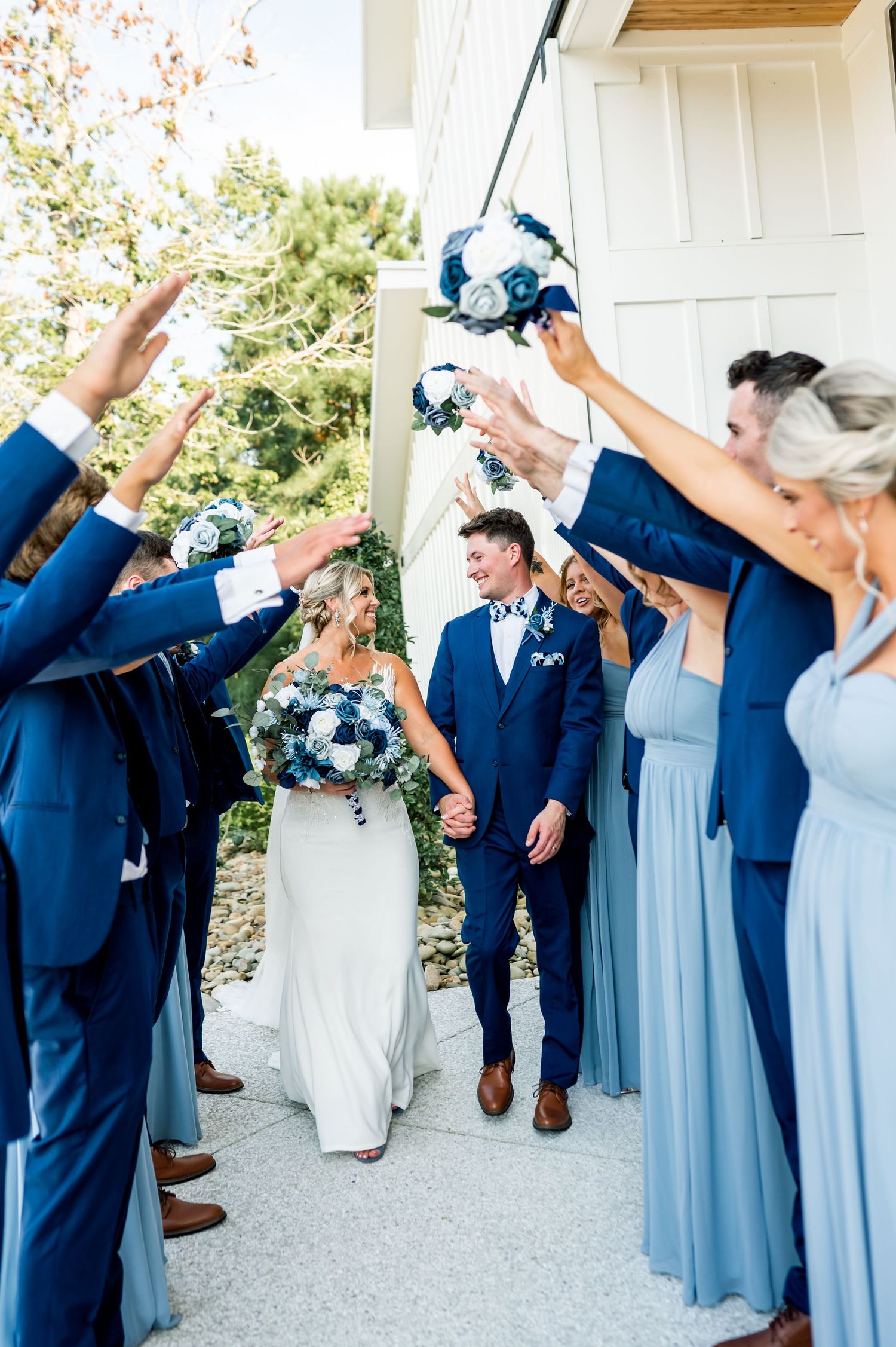Wedding party in navy suits and light blue dresses poses playfully outside.