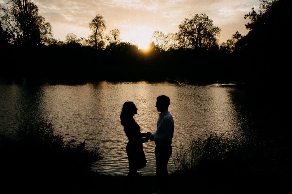 Silhouette of couple holding hands by a lake during a stunning golden sunset.