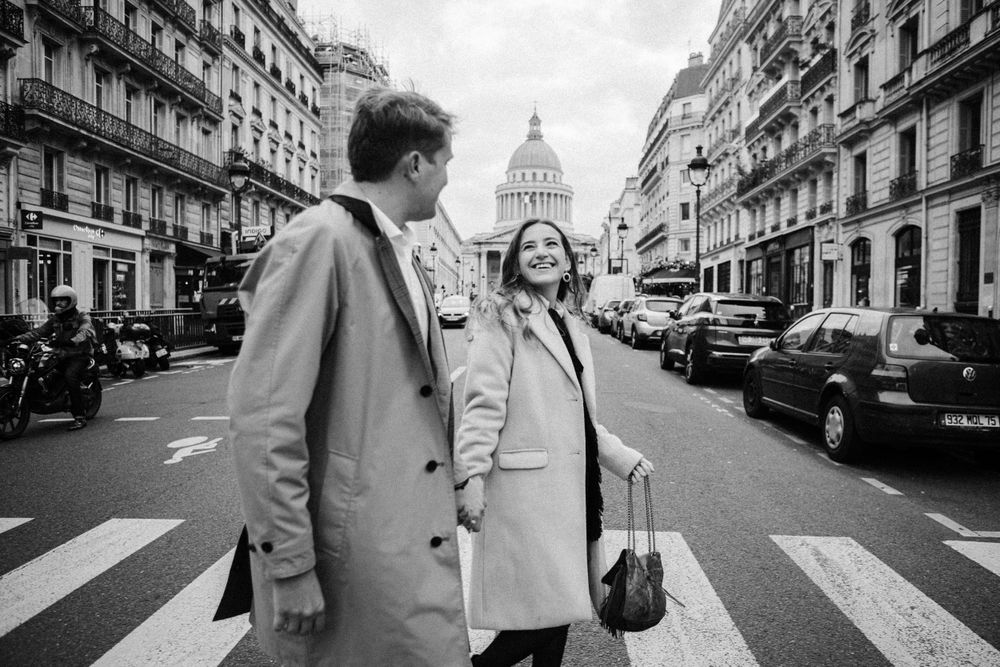 Black and white photo of couple holding hands crossing a Paris street near the Pantheon.