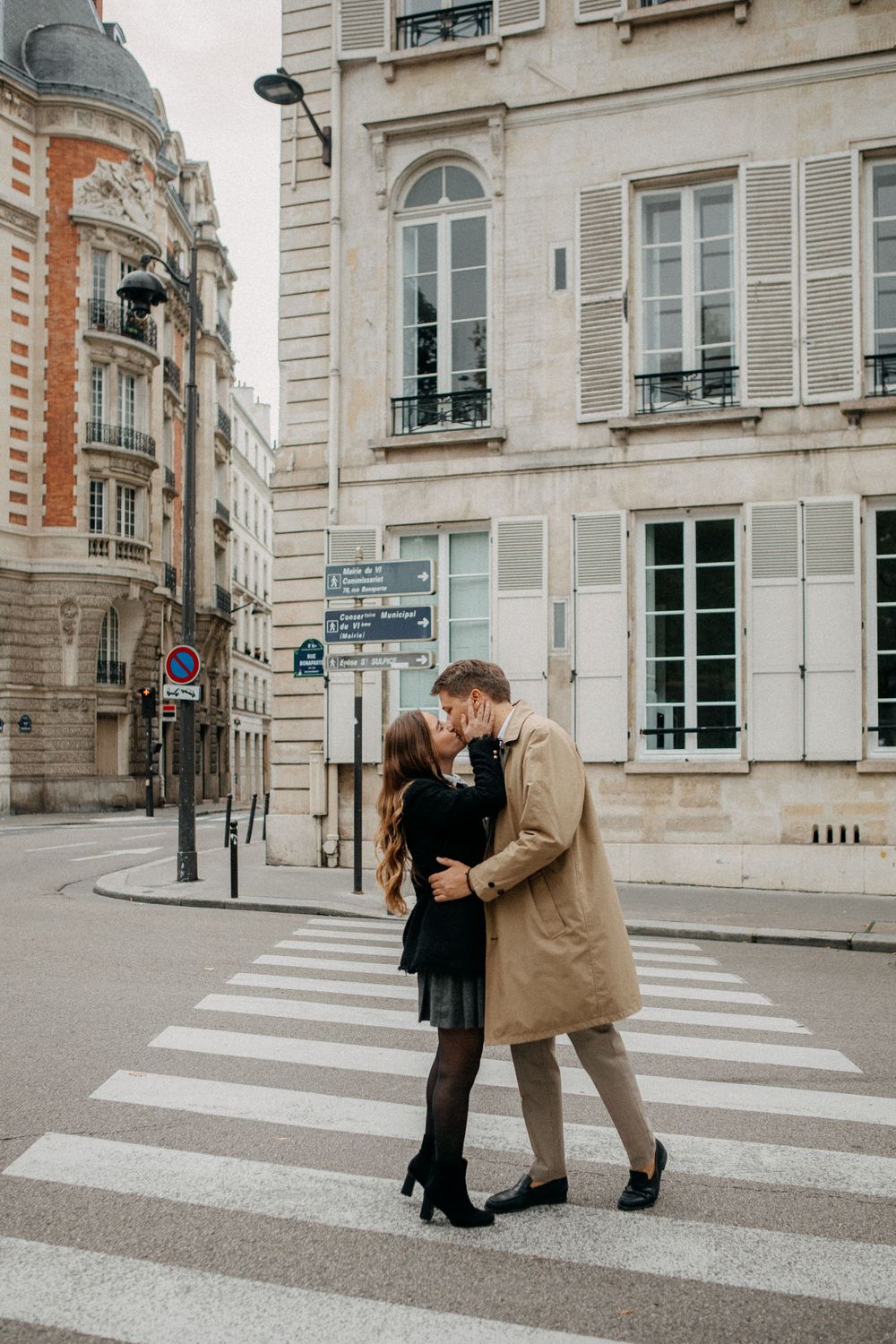Couple sharing a romantic kiss on a zebra crossing in a classic Parisian street setting.