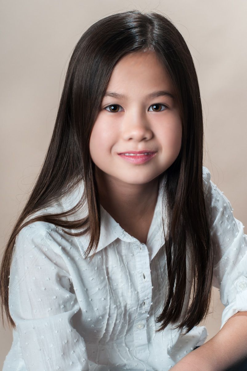 Studio portrait of young girl in white shirt with long dark hair.