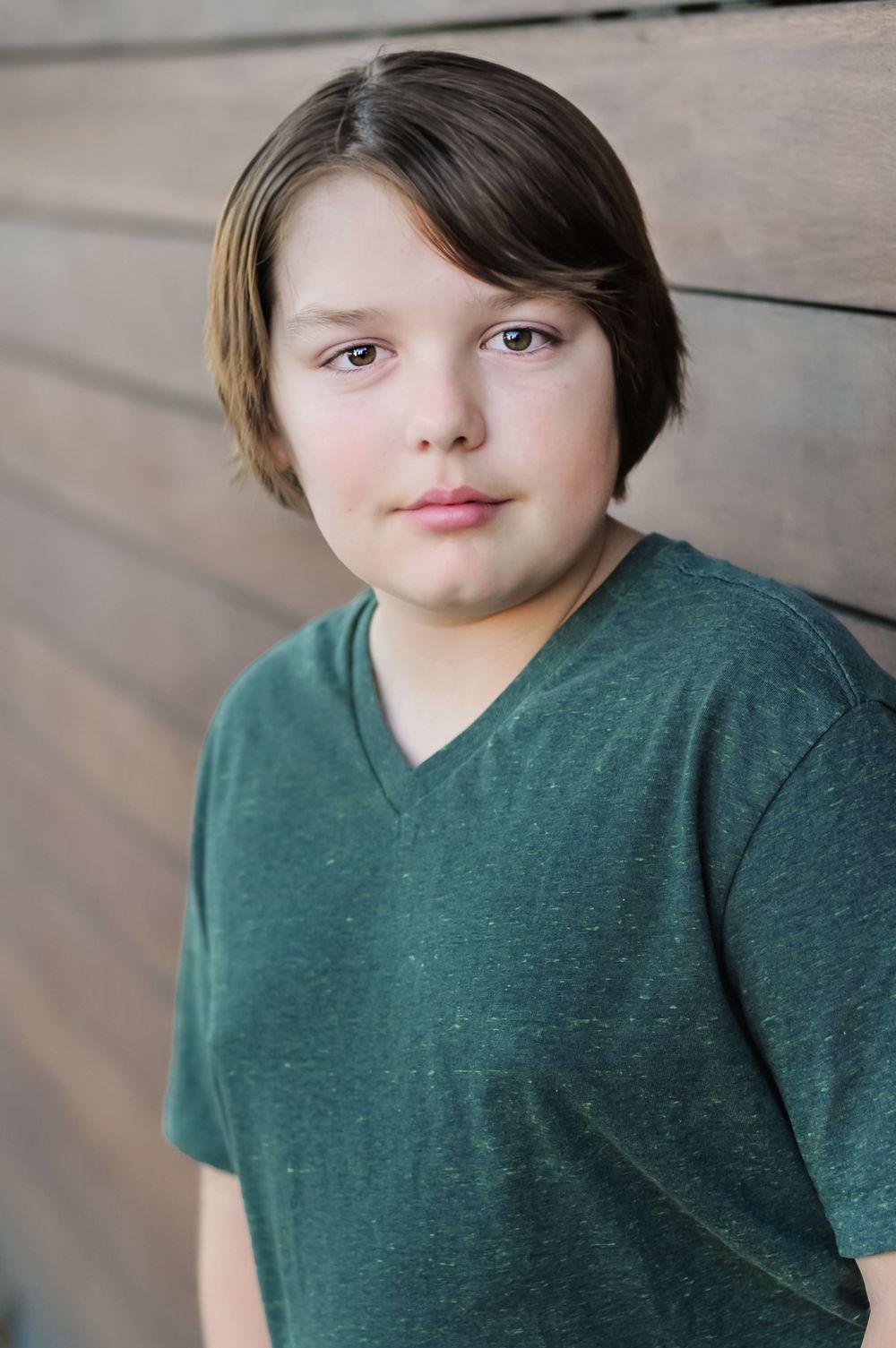 Portrait of youth wearing dark green v-neck t-shirt against wooden wall.