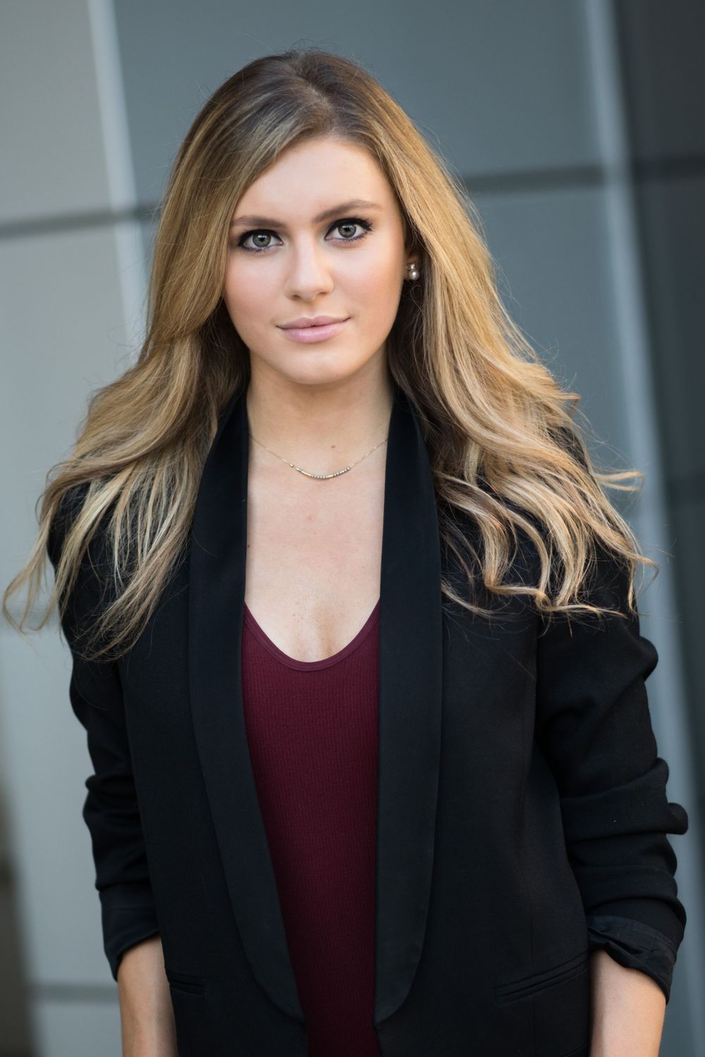 Professional headshot wearing a black blazer and burgundy top with styled blonde hair.