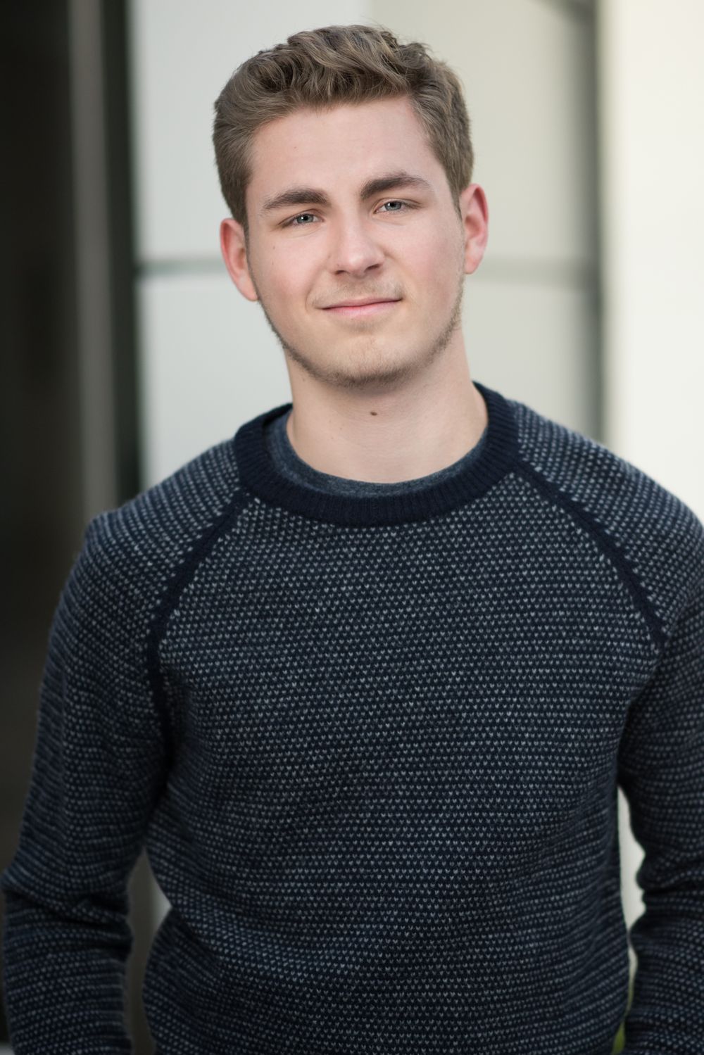 Professional headshot of a young man wearing a dark textured sweater.