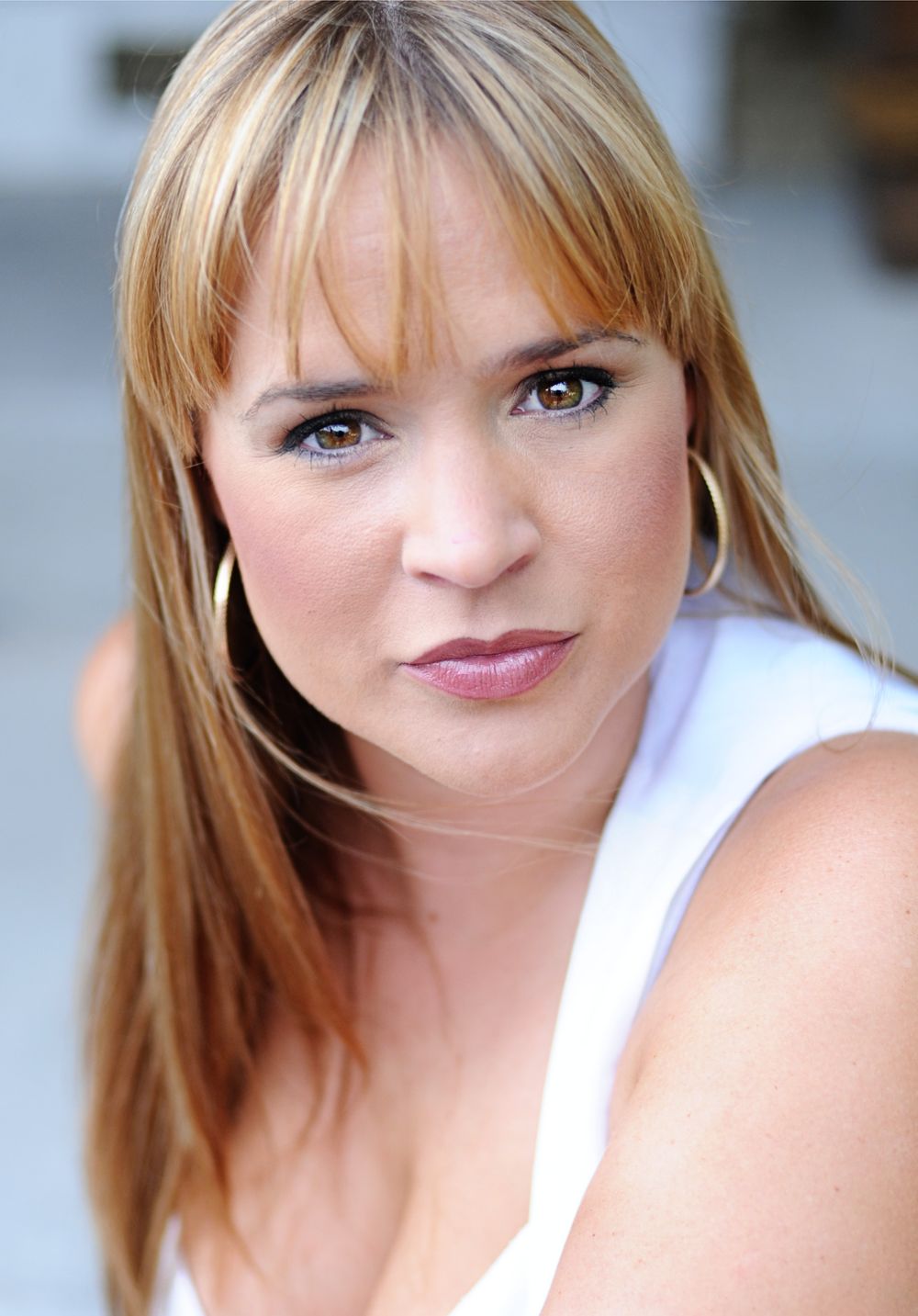 Headshot of blonde woman in white top with natural makeup against light background.