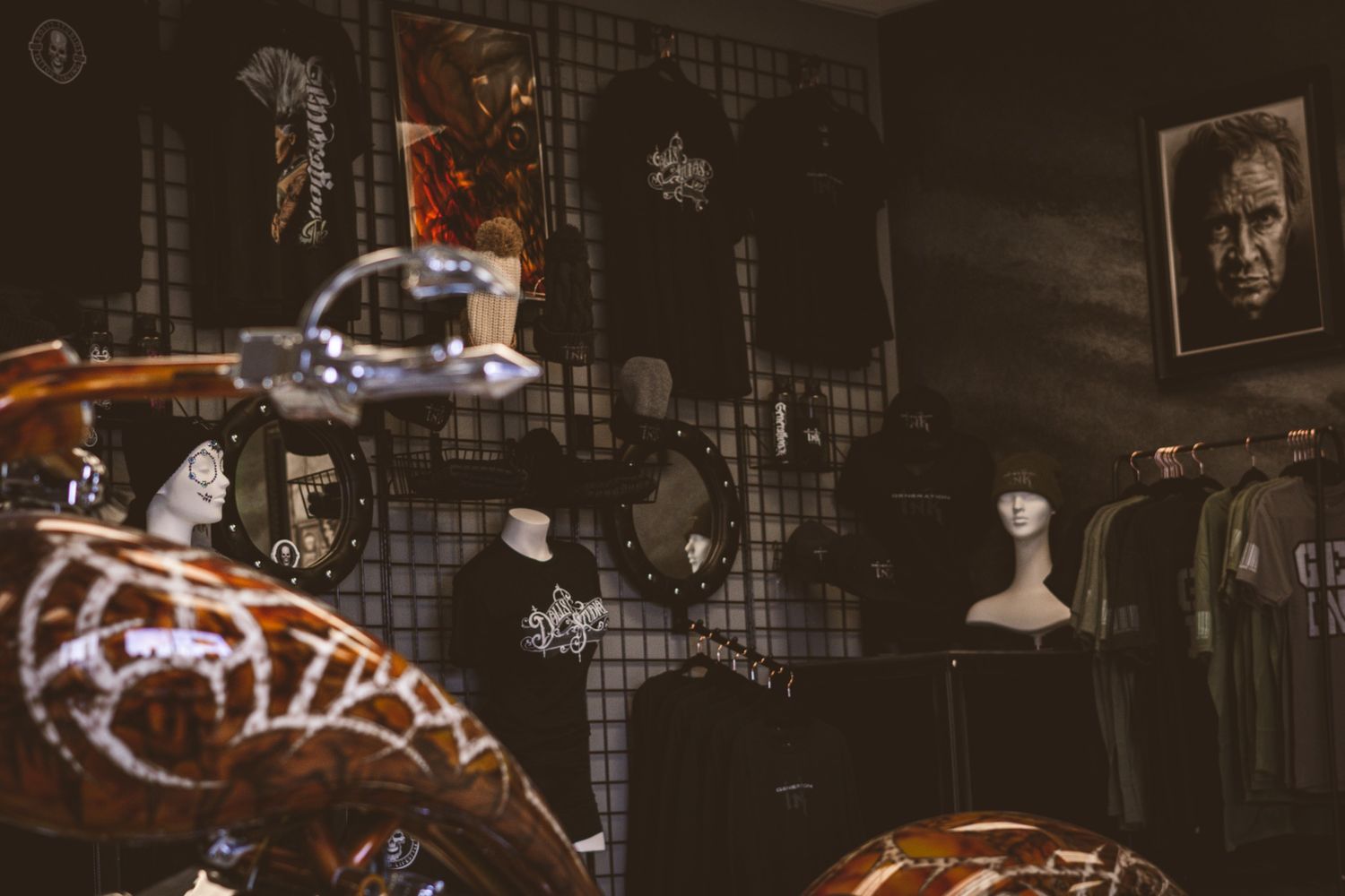 Dark tattoo shop interior with motorcycle, mannequins, apparel, and wall art on display.