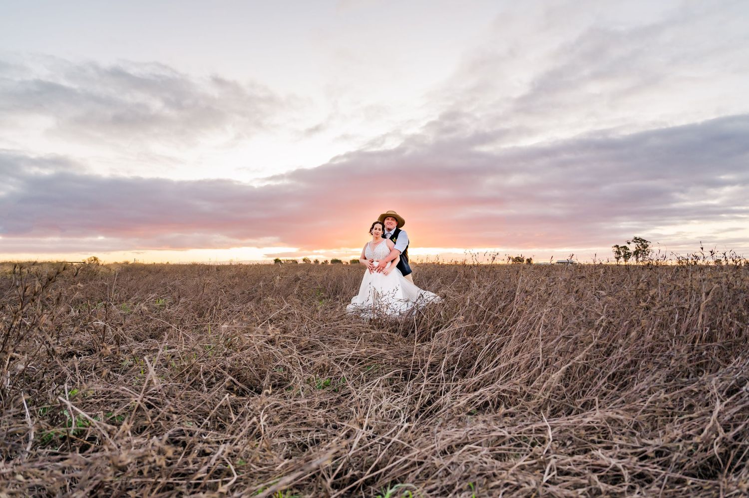 A romantic sunset wedding portrait in a rustic field with dramatic sky overhead.