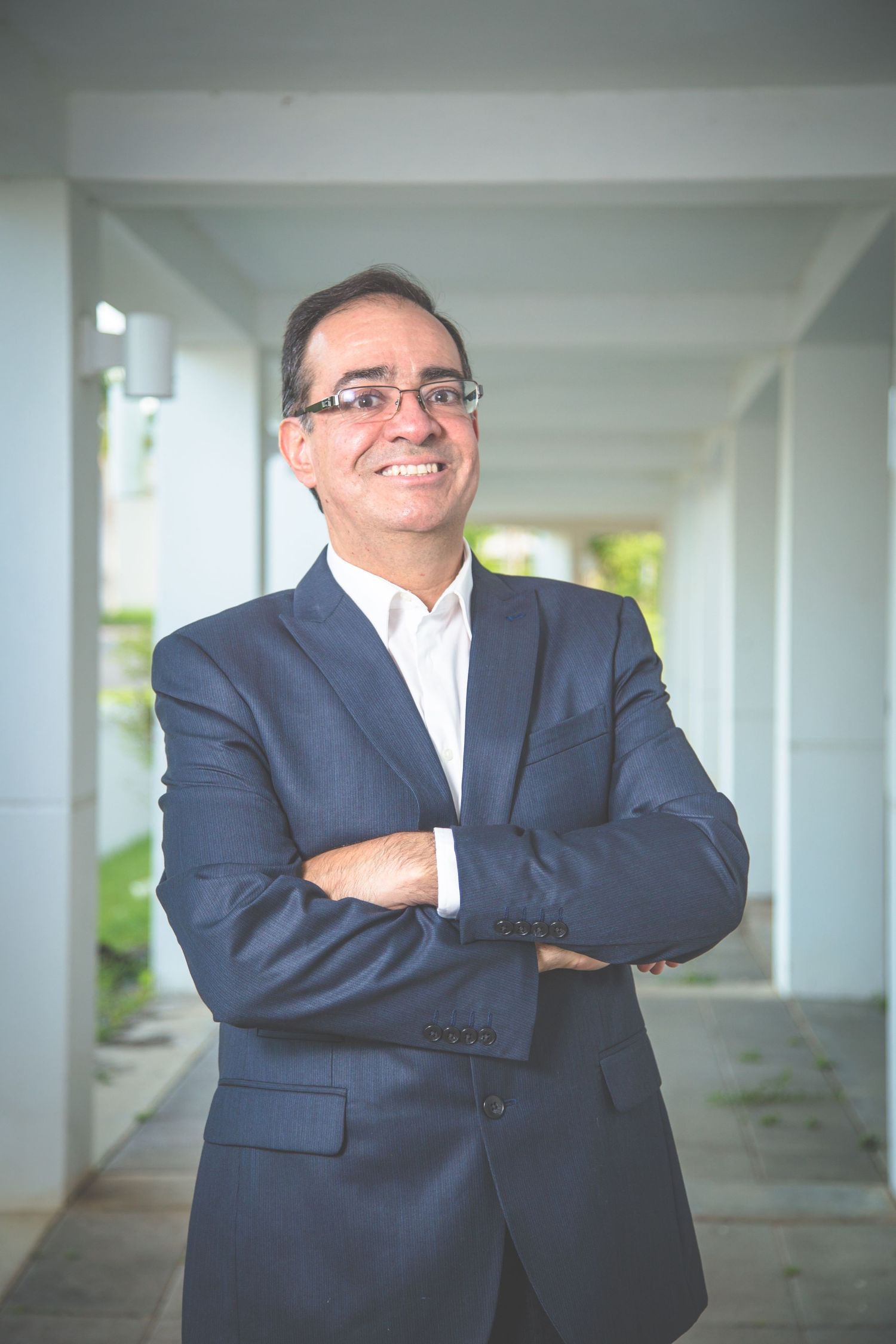 Business professional in dark suit poses in white corridor with natural lighting.