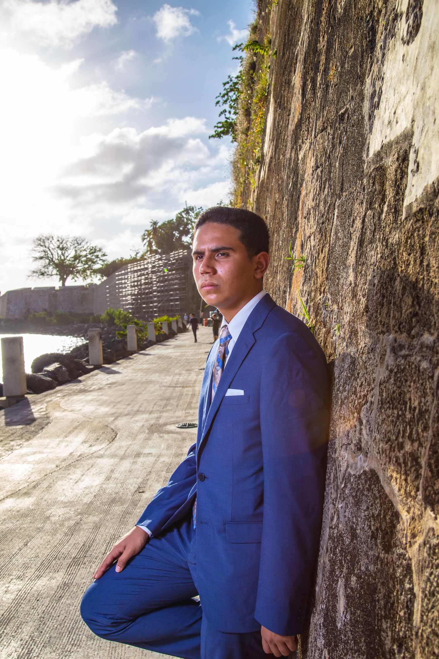 Person in blue business suit poses against stone wall outdoors.