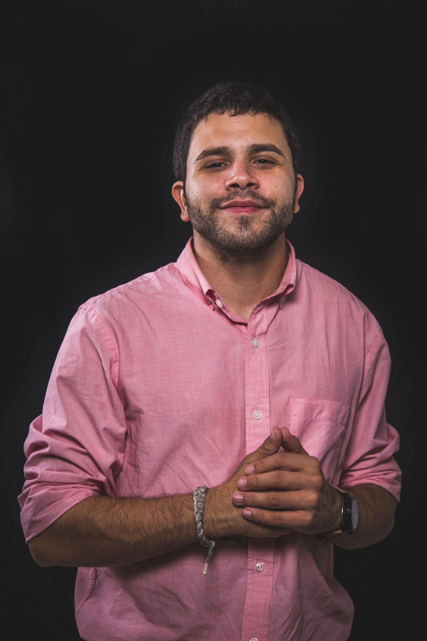 Portrait of person wearing pink button-down shirt against black background.