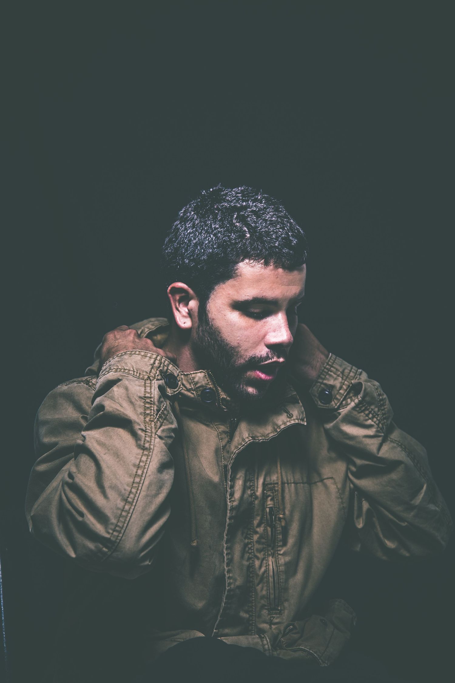 Dramatic portrait of person in brown jacket against dark background.