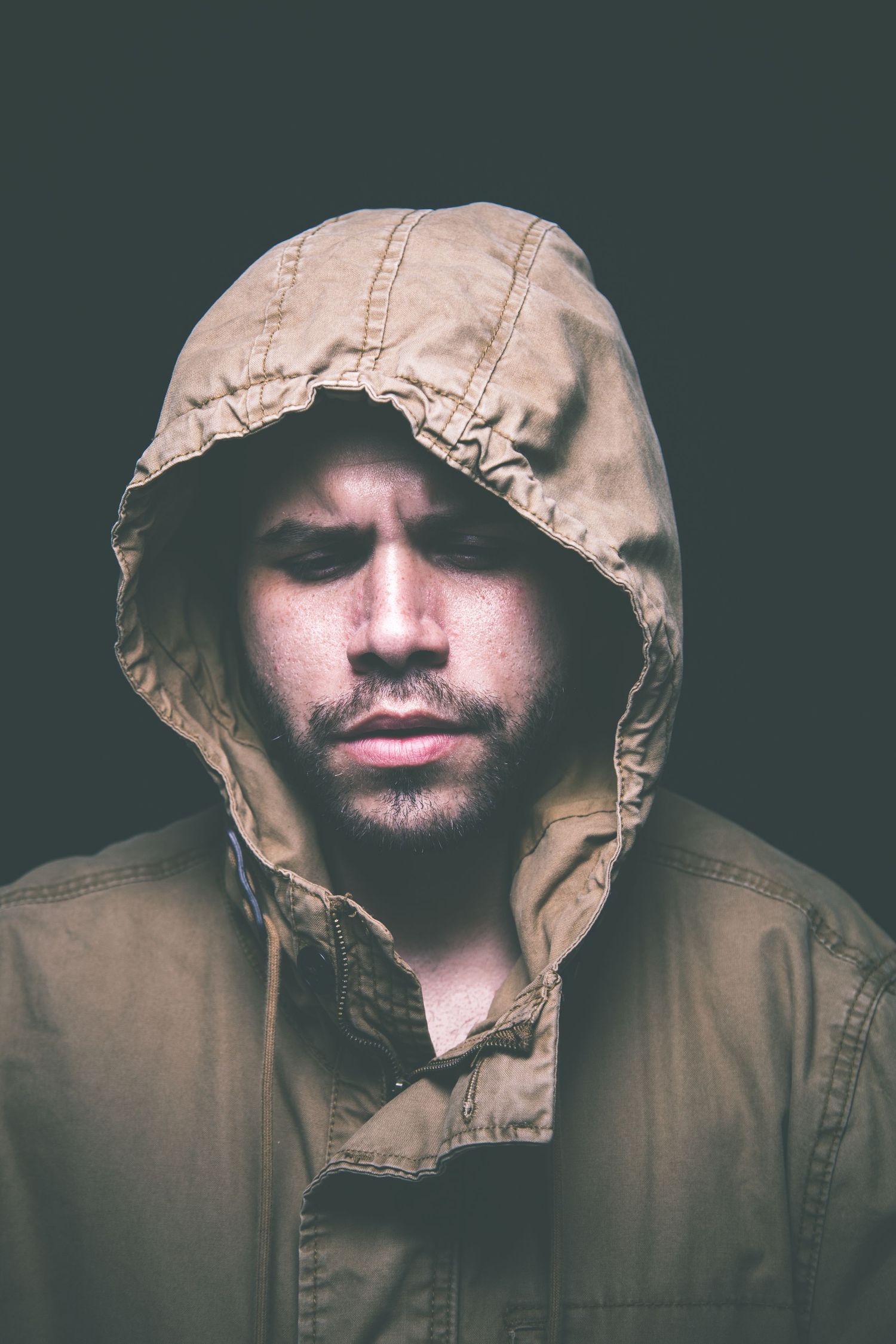 Moody portrait of person wearing tan hooded jacket in shadows.