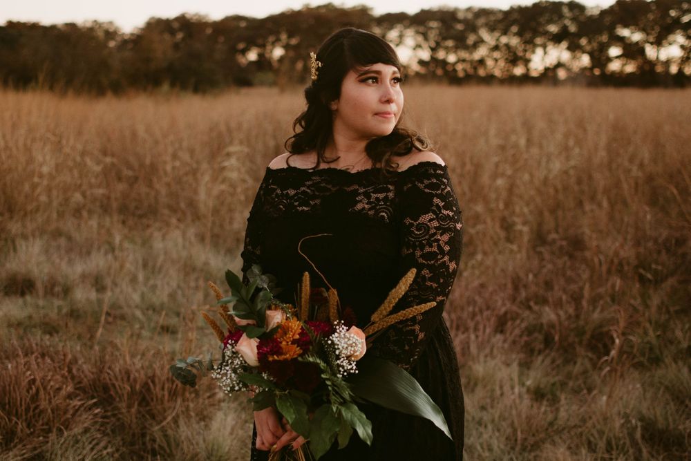 A person in a black lace dress holds an elegant autumn bouquet in a golden field at sunset.
