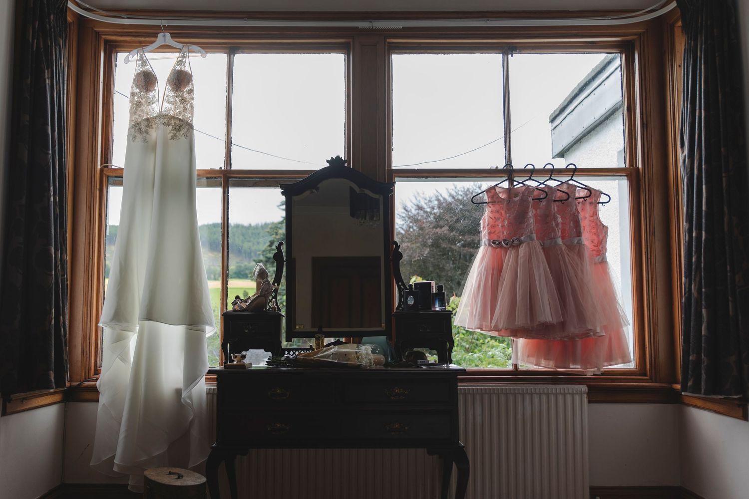 huwelijkskledij hangt aan kapstokken bij het venster in een cottage in Schotland tijdens een destination wedding