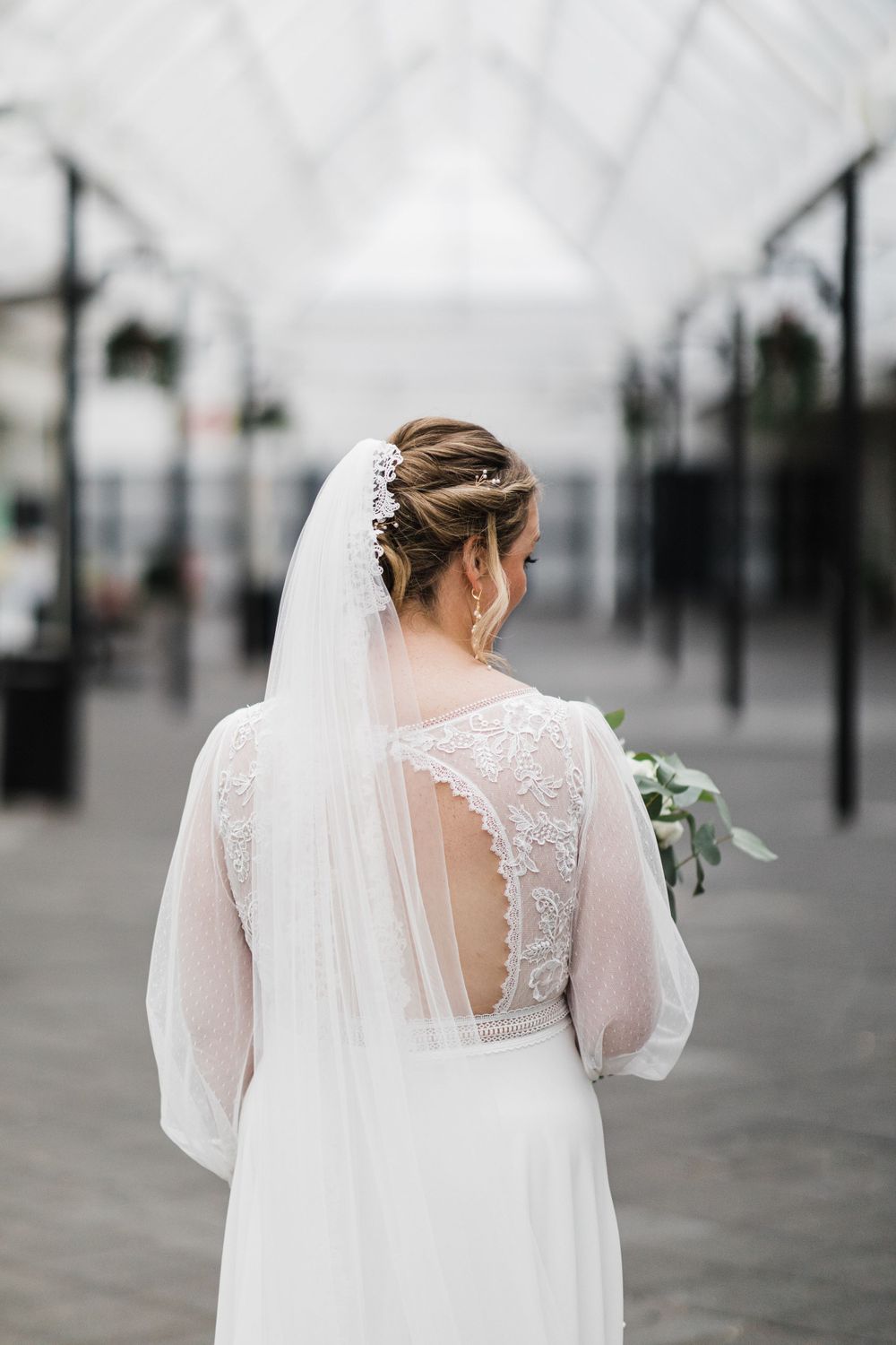 Back view of a bride in a lace detailed dress with sheer back and flowing veil.
