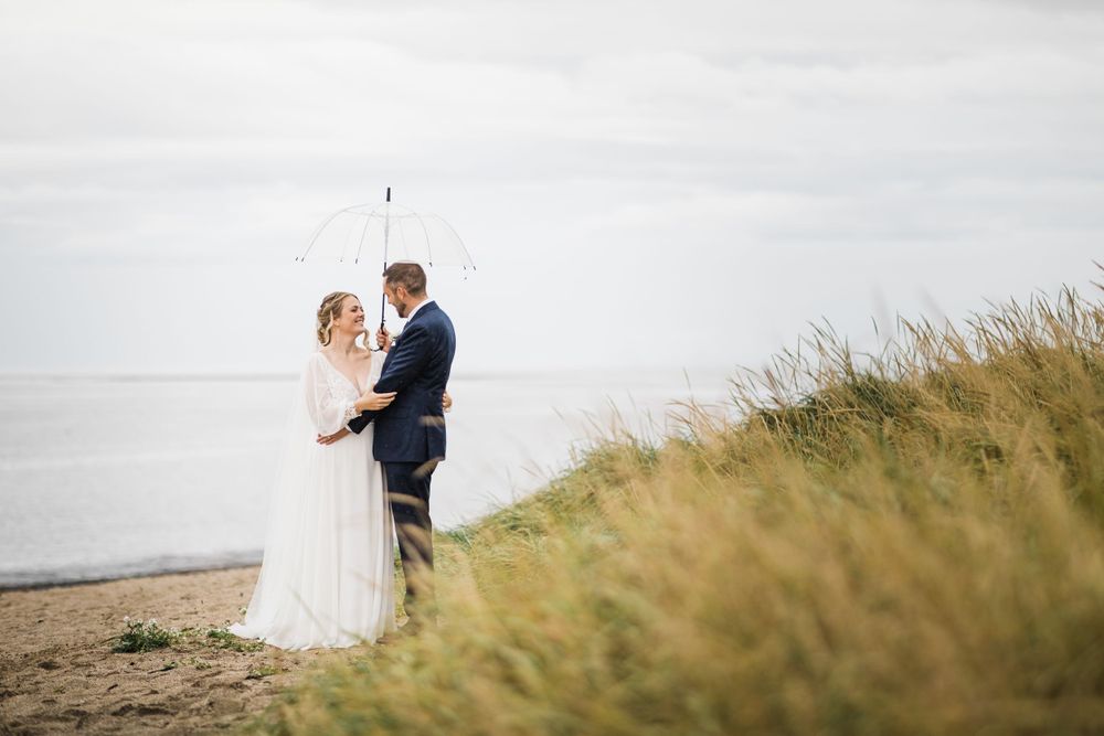 A couple shares a romantic moment on a coastal cliff with tall grass and ocean views.