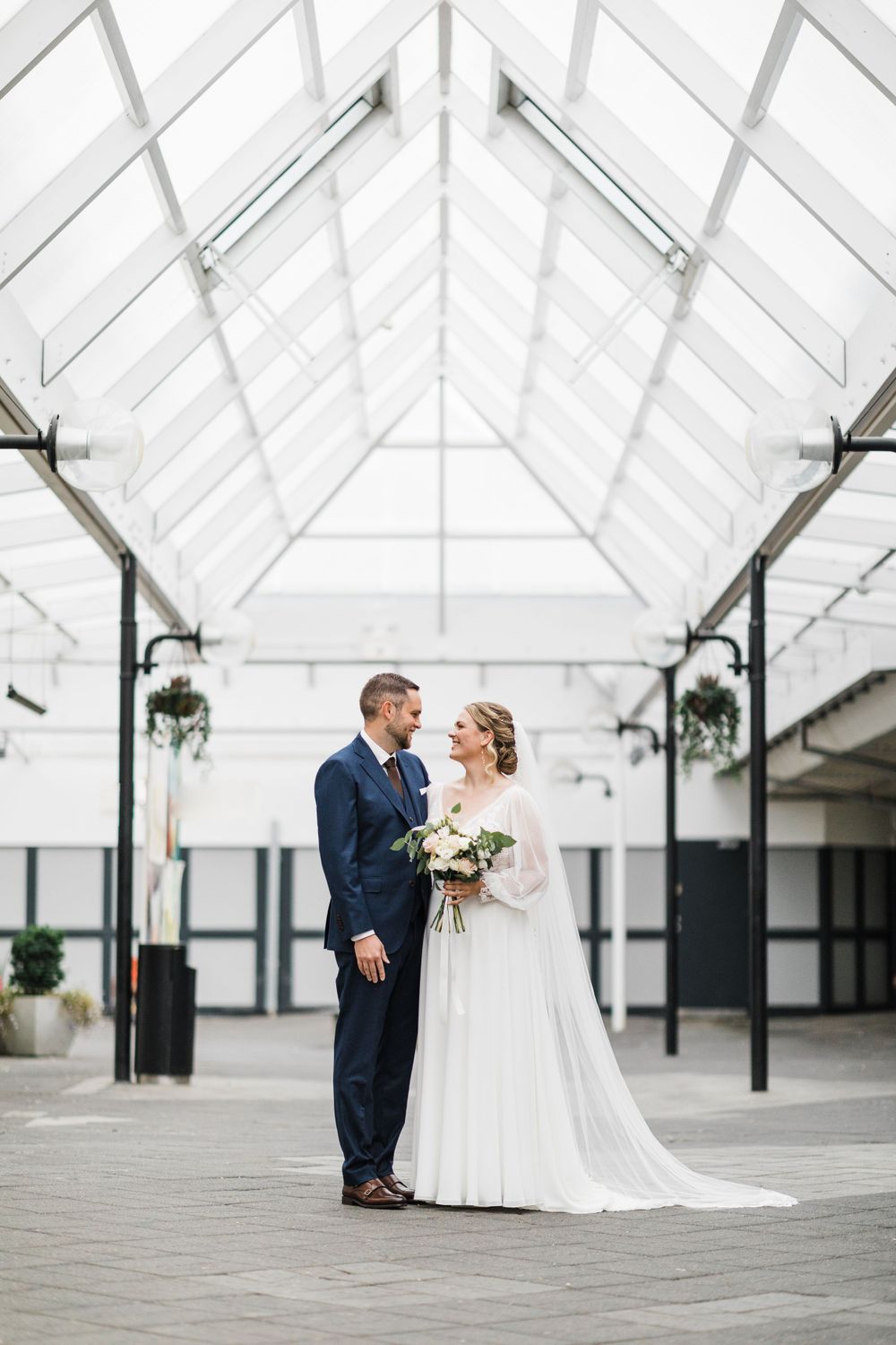 Elegant wedding portrait of a couple under a bright white greenhouse structure.