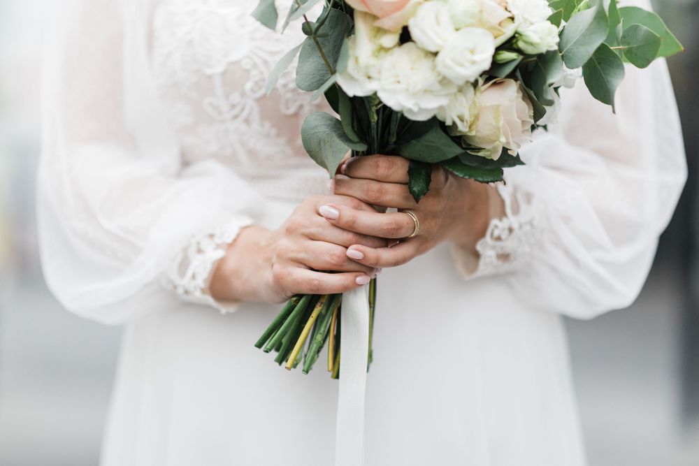 Close-up of hands holding wedding bouquet with white roses and eucalyptus leaves.