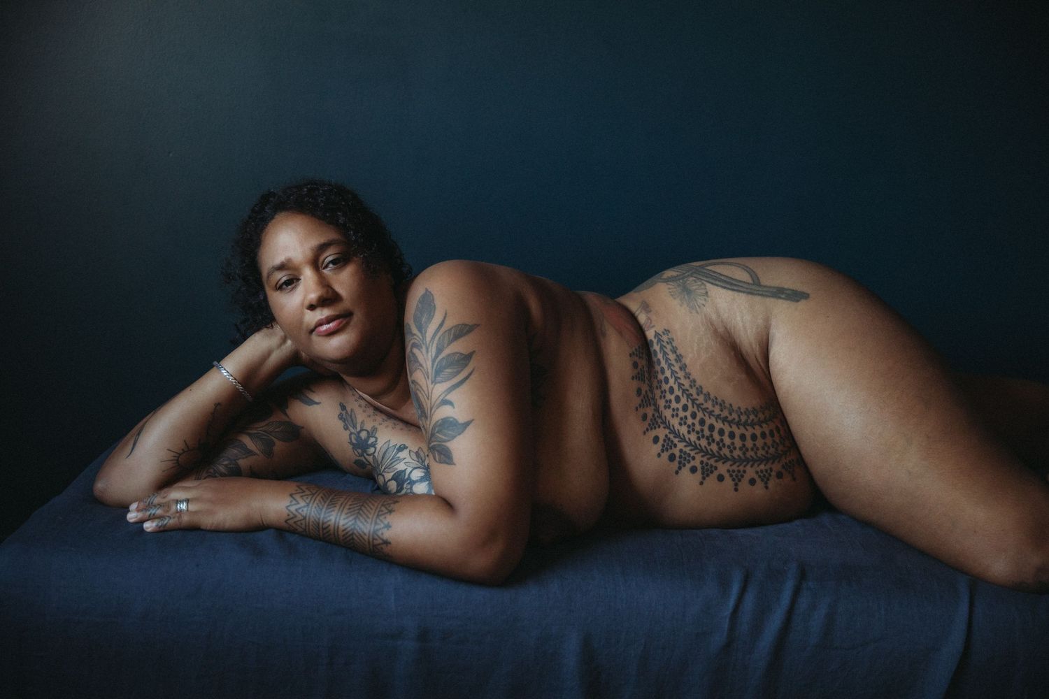 award winning maternity photography by sarah stirk london of pregnant woman laying on couch heavily tattooed