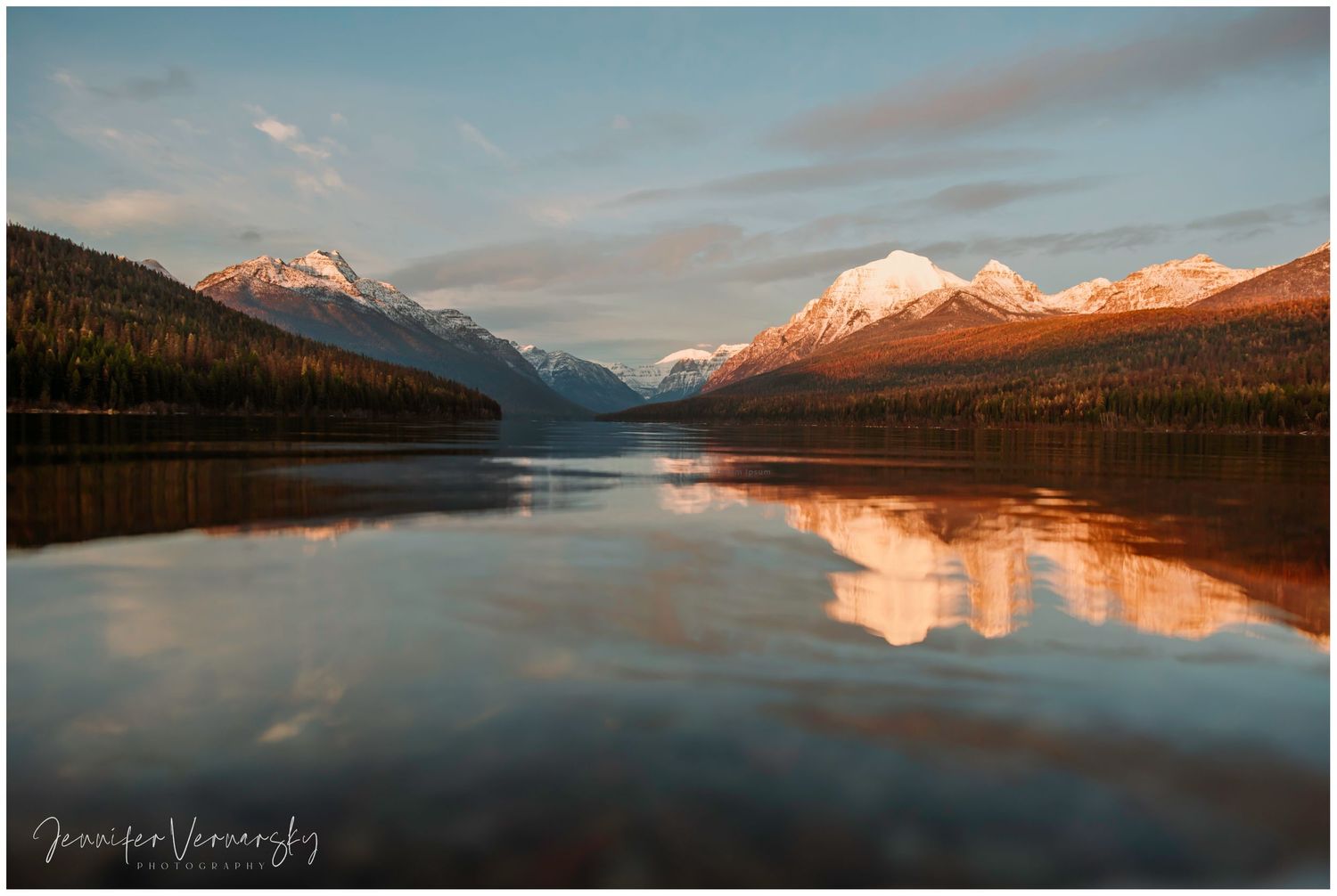 Snow-capped mountains reflected in calm lake waters during a colorful sunset.