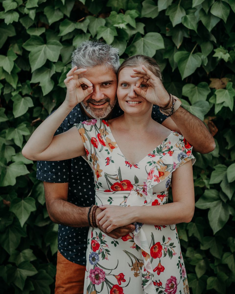 A couple makes silly expressions while posing together against a wall of green ivy leaves.