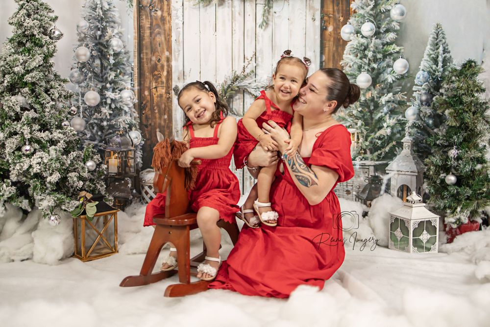Mother and two daughters in matching red dresses pose with Christmas trees and holiday decor.