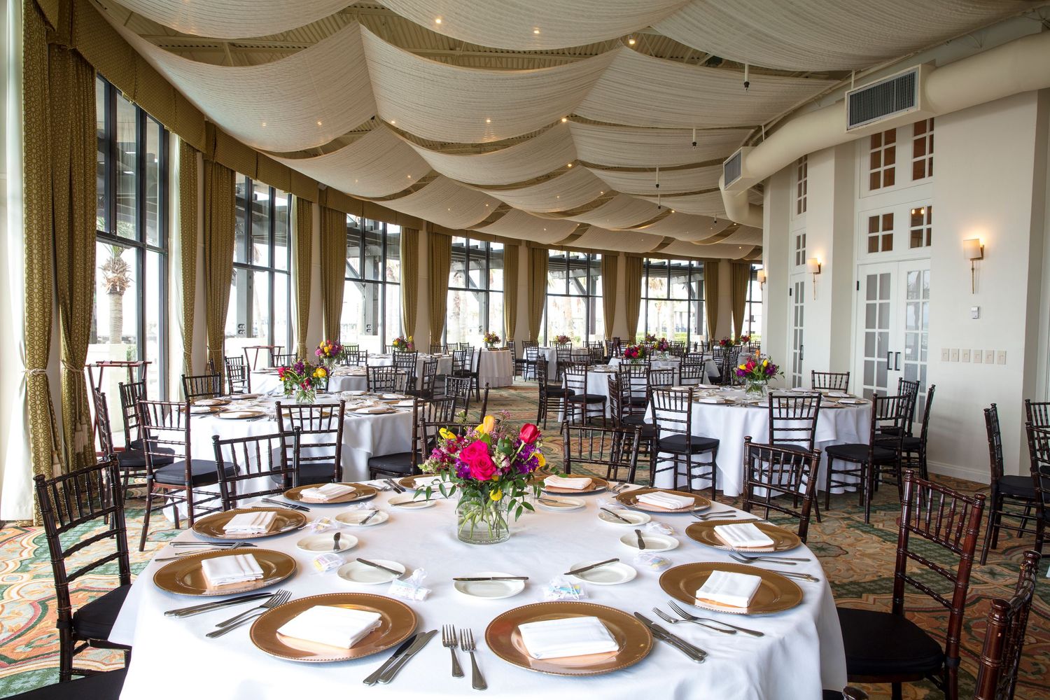 Grand ballroom with draped ceiling and elegant table settings features romantic ambient lighting.