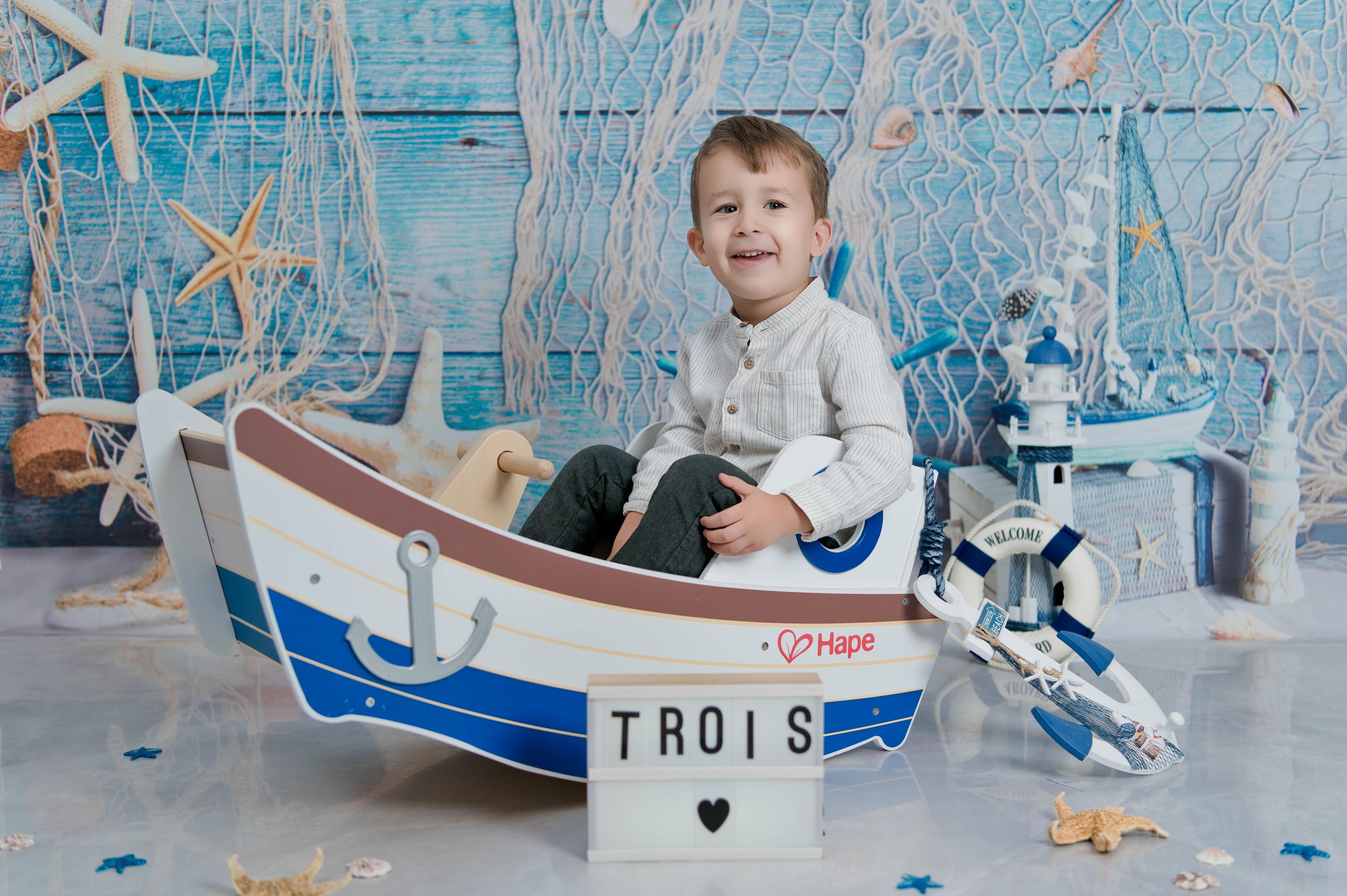 Small decorative boat prop with nautical themed background featuring starfish and ship wheel decor.