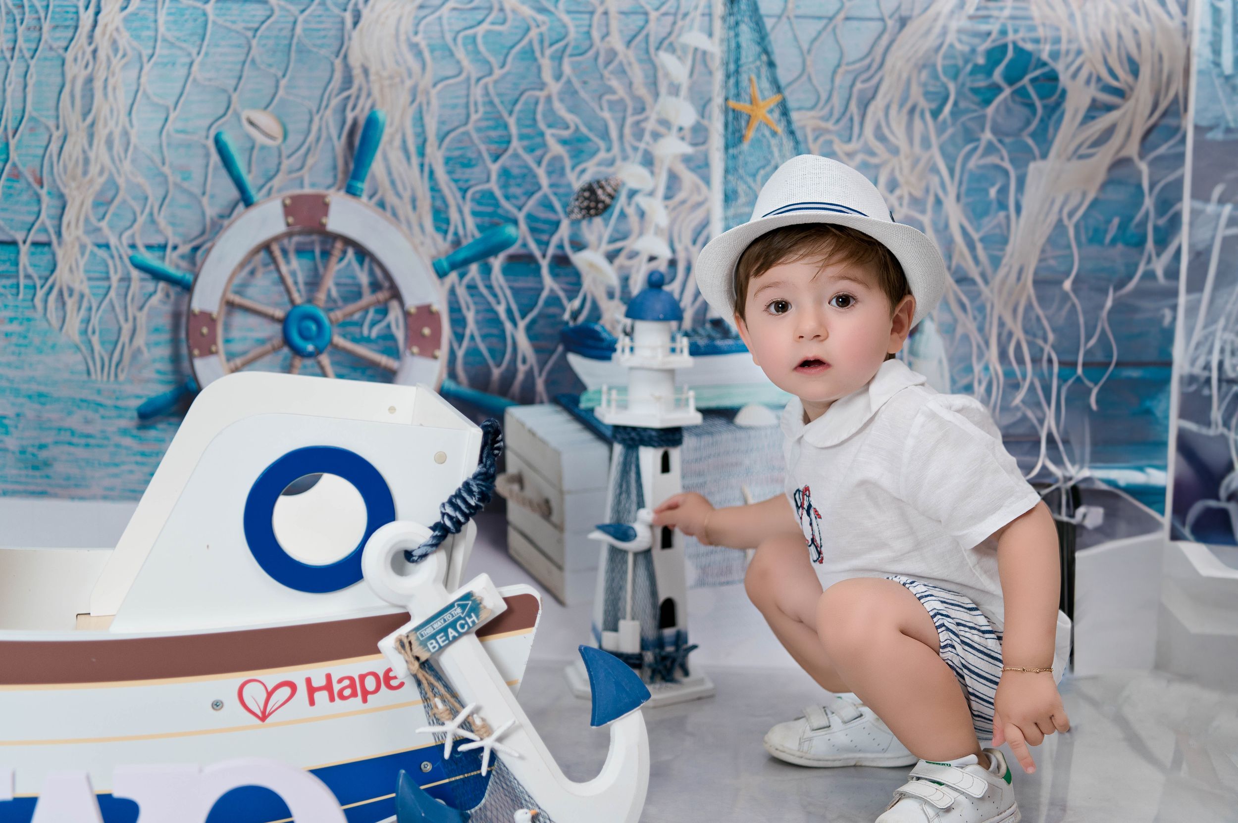 Nautical themed photo setup with boat wheel, lighthouse, and white decorative elements.