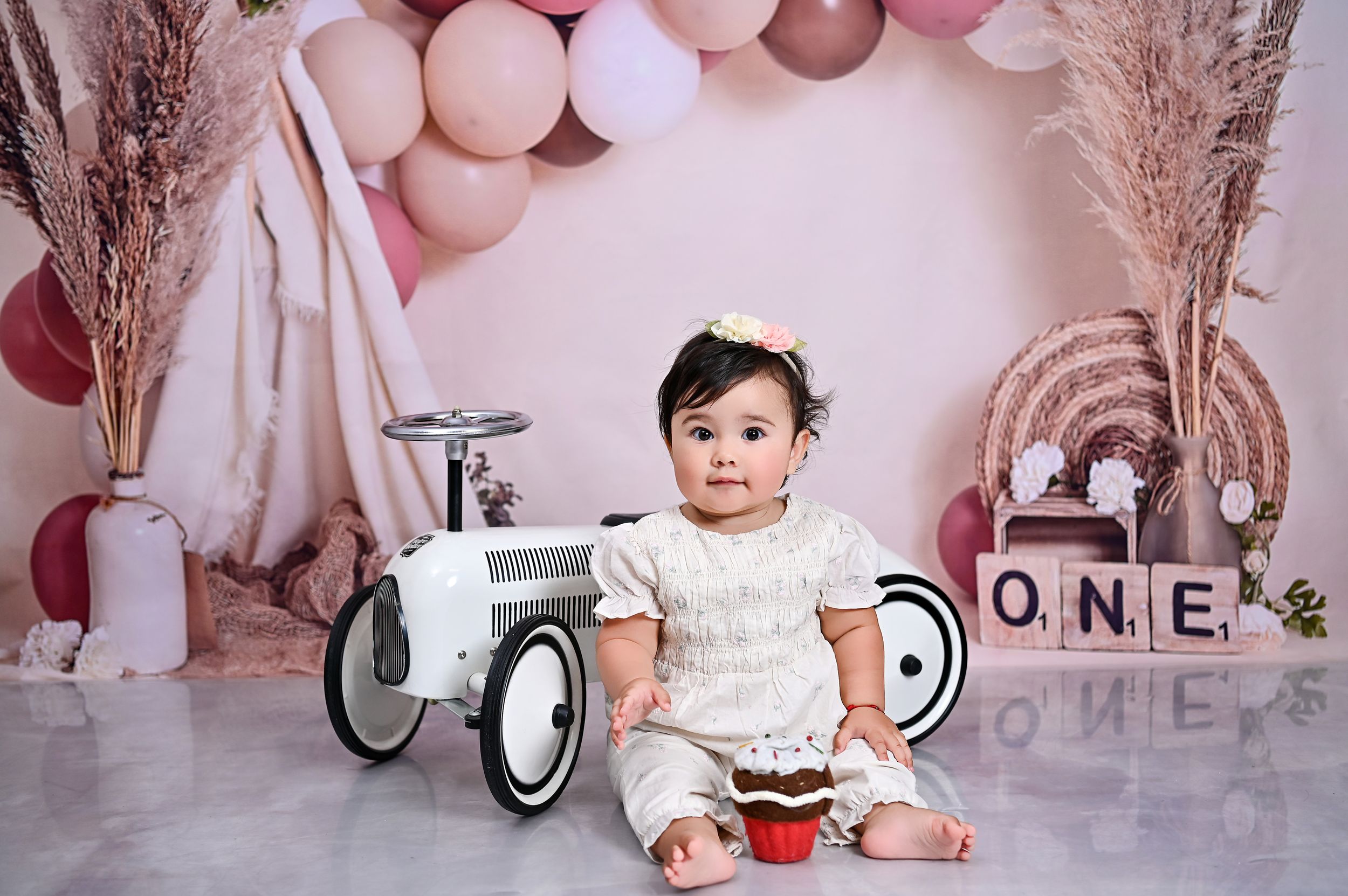 Pink balloon arch with vintage ride-on car and ONE letter blocks in soft nursery setting.