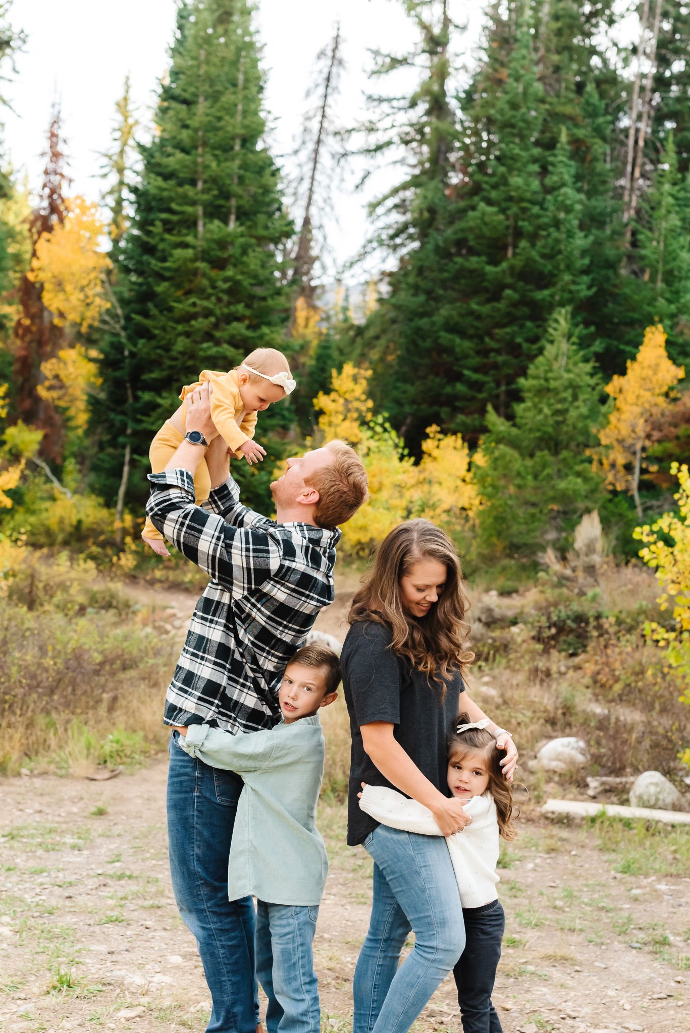 Family sharing playful moments together in a mountain setting with evergreen trees and fall colors.