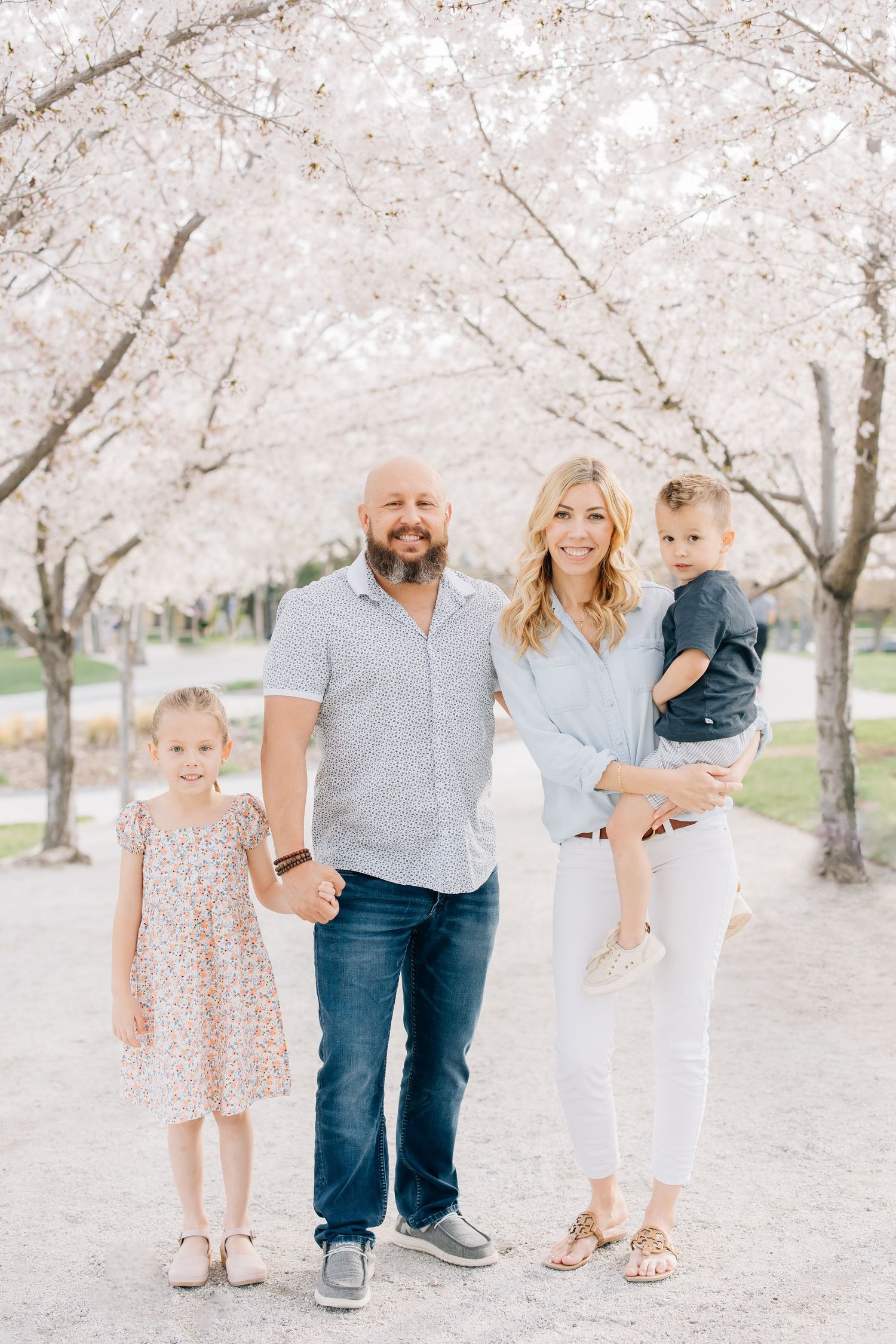 Family of four at the capitol building on a gravel trail lined with trees, smiling at the camera.