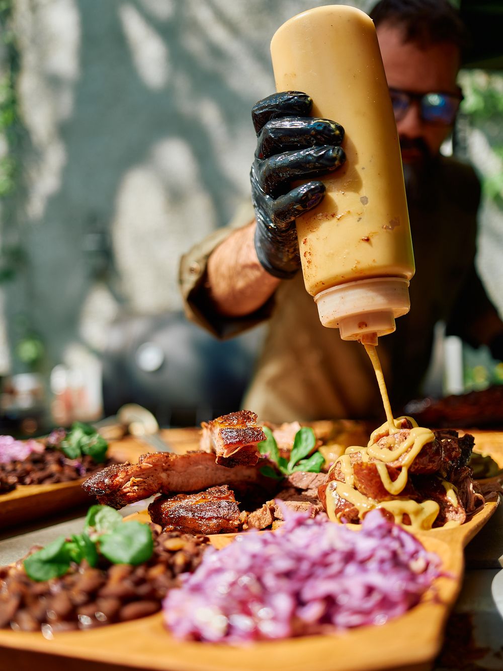 Squeezing yellow sauce onto plated barbecue meat with black gloved hands.